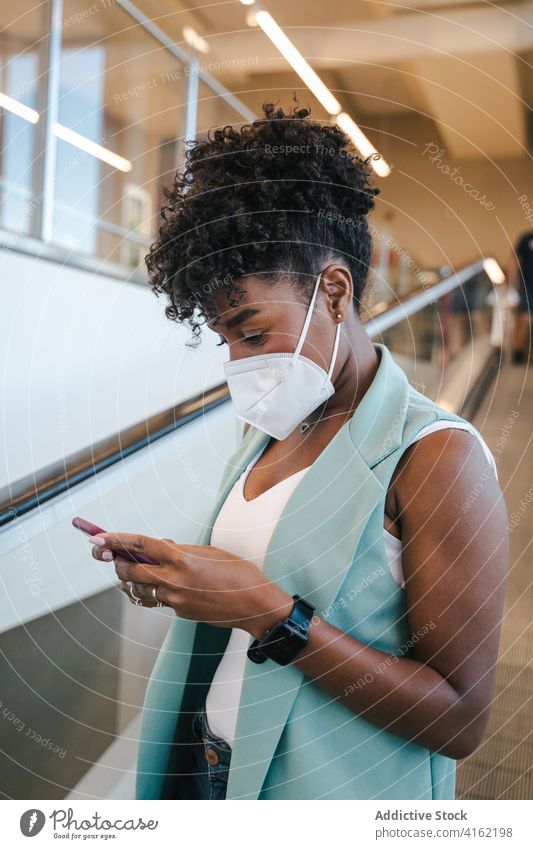 Fröhliche ethnische Frau mit Maske und Smartphone Mundschutz COVID Coronavirus Pandemie neue Normale Sicherheit positiv jung Afroamerikaner schwarz Mobile