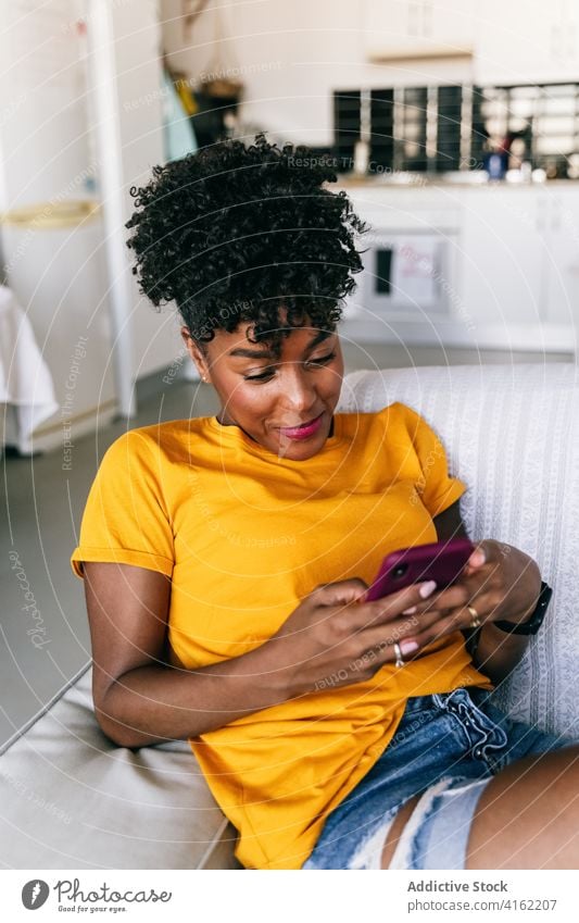 Lachende schwarze Frau, die ein Smartphone zu Hause benutzt benutzend heimwärts Spaß haben aufgeregt Browsen Mobile heiter tausendjährig jung Jugendlicher