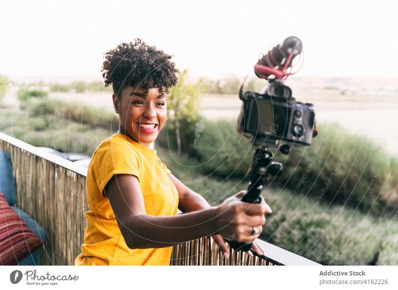 Positive Bloggerin dreht Video auf Terrasse vlog Selfie-Stick Fotokamera Aufzeichnen heiter reisen schießen Glück jung Frau Afroamerikaner schwarz ethnisch