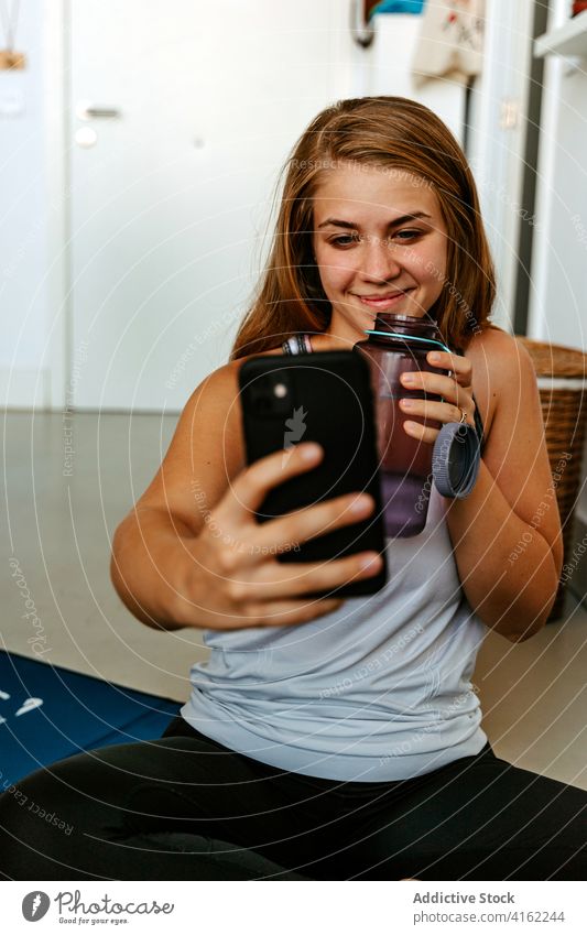 Zufriedene Sportlerin mit Wasserflasche, die ein Selfie mit ihrem Smartphone macht Vitalität Energie Training Lächeln Inhalt Hydrat Getränk üben Flasche