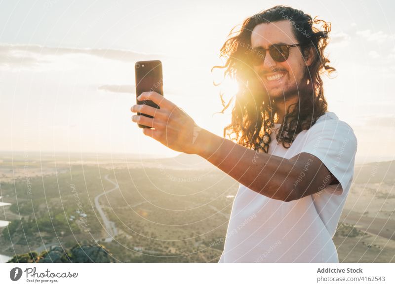 Fröhlich Mann unter Selfie gegen sonnigen üppigen Tal Reisender heiter Zahnfarbenes Lächeln Smartphone Natur aufgeregt Moment Apparatur Bergkuppe Fernweh reisen