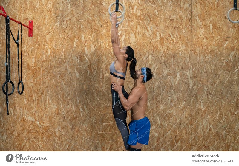 Anonymer Trainer, der eine weiße Sportlerin aufzieht, die an Ringen im Fitnessstudio trainiert Trainerin Hilfsbereitschaft operativ Training gymnastisch