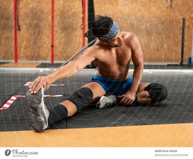 Sportler streckt die Beine beim Training im Fitnessstudio Dehnung Übung muskulös beweglich Gesunder Lebensstil Sporthalle Mann Turnschuh sitzen Stock Muskel