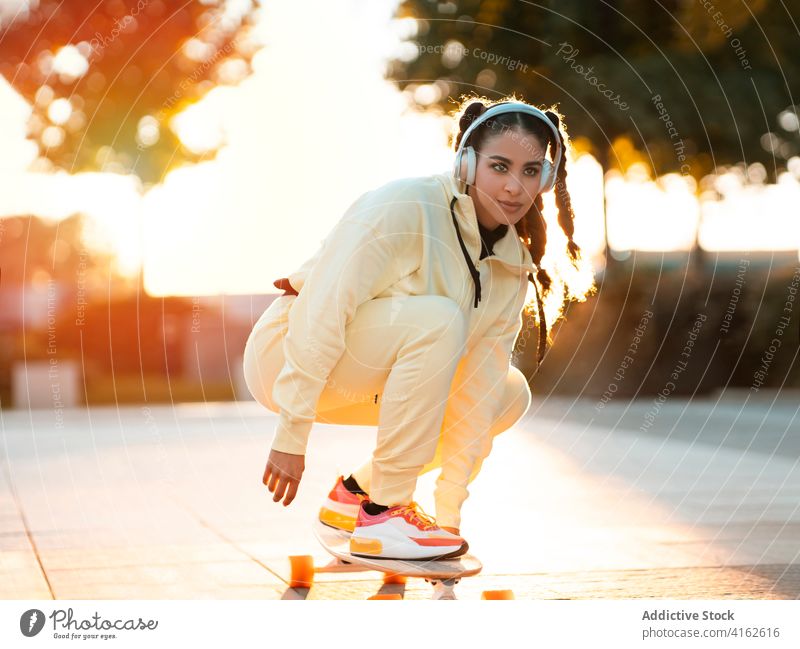 Trendige weibliche Millennials hören Musik beim Longboardfahren im Park Frau Mitfahrgelegenheit zuhören positiv aktiv trendy Freude modern Sonnenuntergang jung