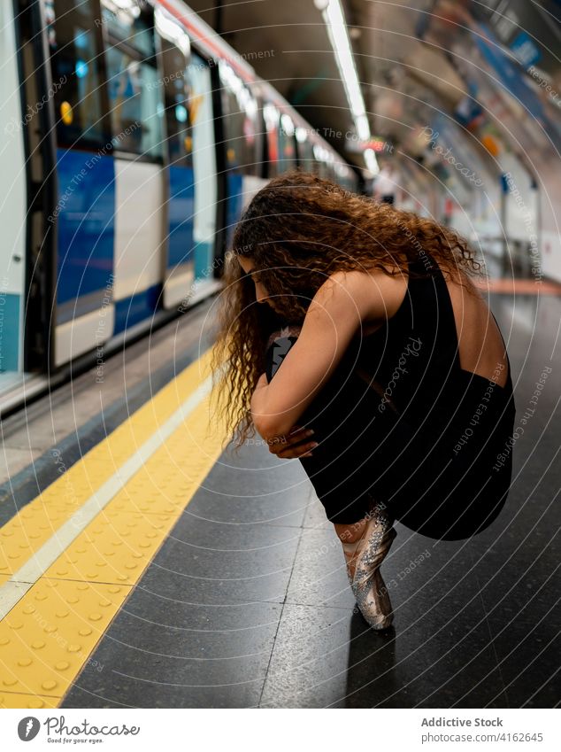 Anonyme junge Ballerina auf Zehenspitzen auf einem U-Bahn-Bahnsteig sitzend Frau Knie umarmend Voute Station ausführen Melancholie Anmut Stil Zug lange Haare