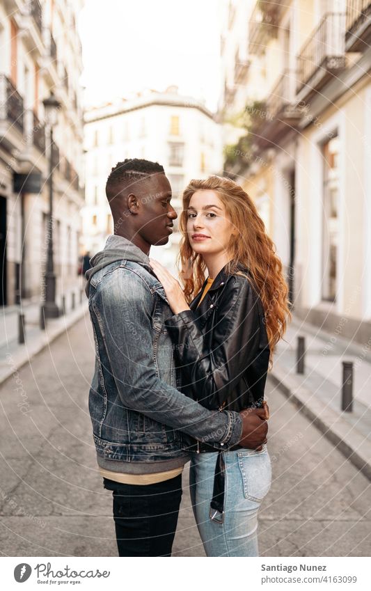 Liebendes multiethnisches junges Paar in die Kamera schauen Stehen Straße umarmend Vorderansicht Porträt Partnerschaft multirassisch Schwarzer Mann Kaukasier