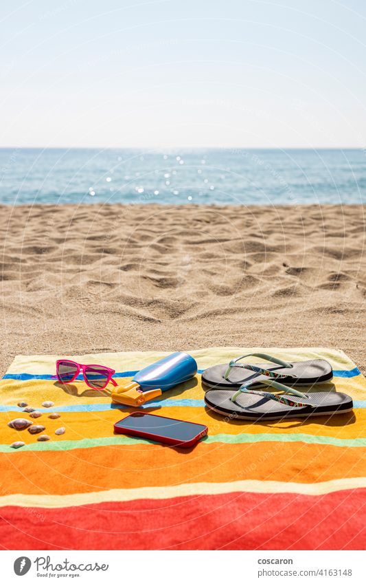 Handtuch, Sonnencreme, Flip-Flops, Sonnenbrille und Smartphone am Strand. Konzept für den Sommer. Zubehör Accessoire blau Flasche farbenfroh Sahne Mode