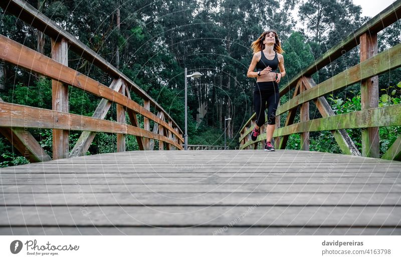 Frau rennt durch einen städtischen Park Sportlerin rennen müde anstrengen Holzsteg Ausdauer durchhalten Beständigkeit entschlossen Stadtpark Athlet heiter