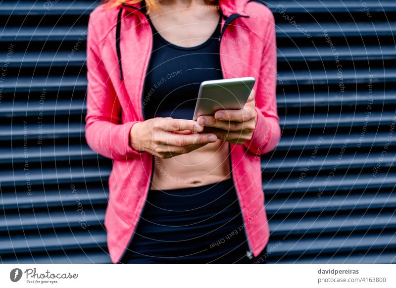 Unerkennbare Sportlerin mit Mobiltelefon unkenntlich Frau Athlet Mittelteil Gitterrost-Hintergrund Handy Porträt Körper Fitness Smartphone Gesundheit Lifestyle
