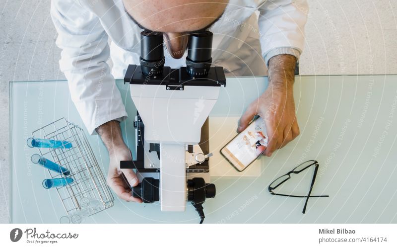 Reife Wissenschaftler männlich trägt einen Laborkittel Blick durch ein Mikroskop in einem Labor. Wissenschaftliches Konzept. wissenschaftlich Kompetenz