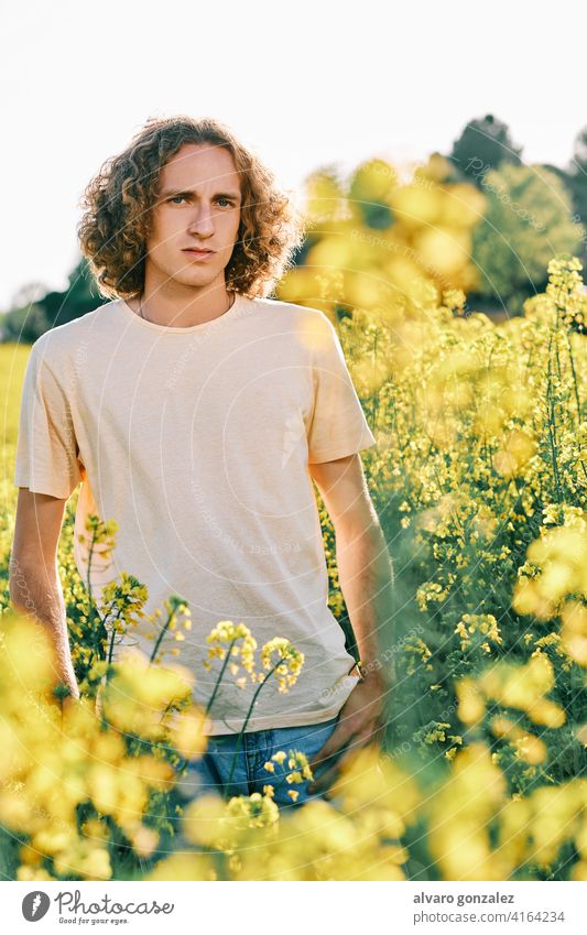 ein junger Mann umgeben von gelben Blumen an einem sonnigen Frühlingstag Raps Natur Landschaft che männlich Porträt Typ gutaussehend Person attraktiv Kaukasier