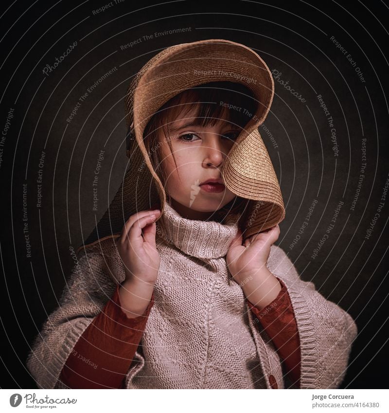 4 Jahre altes kaukasisches Mädchen mit Hut und einem Stoffponcho. Sie posiert stilvoll und elegant und hält den Hut mit ihren Händen. quadratisches Format