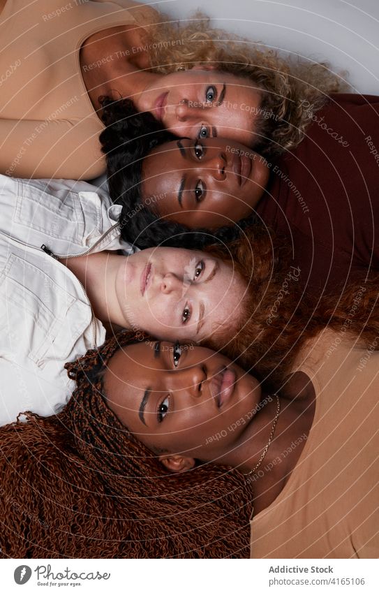 Multirassische Frauen in Reihe liegend im Studio Zusammensein Lügen Model Pastell Farbe Outfit krause Haare multiethnisch rassenübergreifend vielfältig schwarz