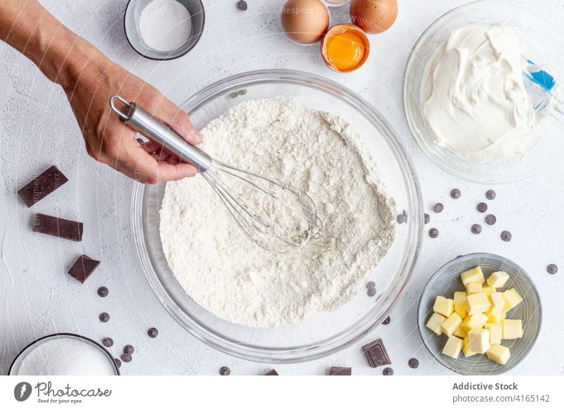 Crop unerkennbar Koch Schneebesen Mehl in Schüssel Person Küchenchef Prozess Werkzeug Bestandteil kulinarisch vorbereiten backen Rezept Produkt Zusammensetzung