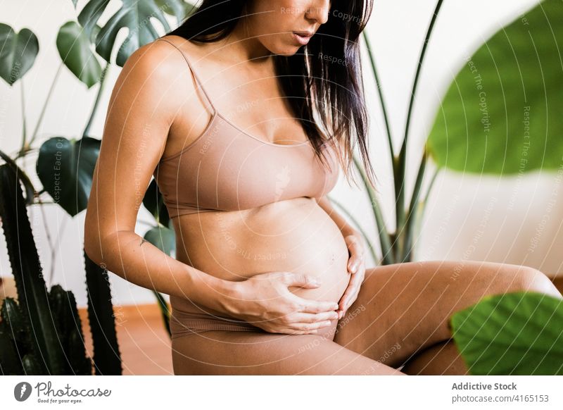 Zarte schwangere Frau, die ihren Bauch im Zimmer berührt Unterwäsche Dessous pränatal Schwangerschaft filigran berühren Angebot Hocker Raum grün erwarten Magen