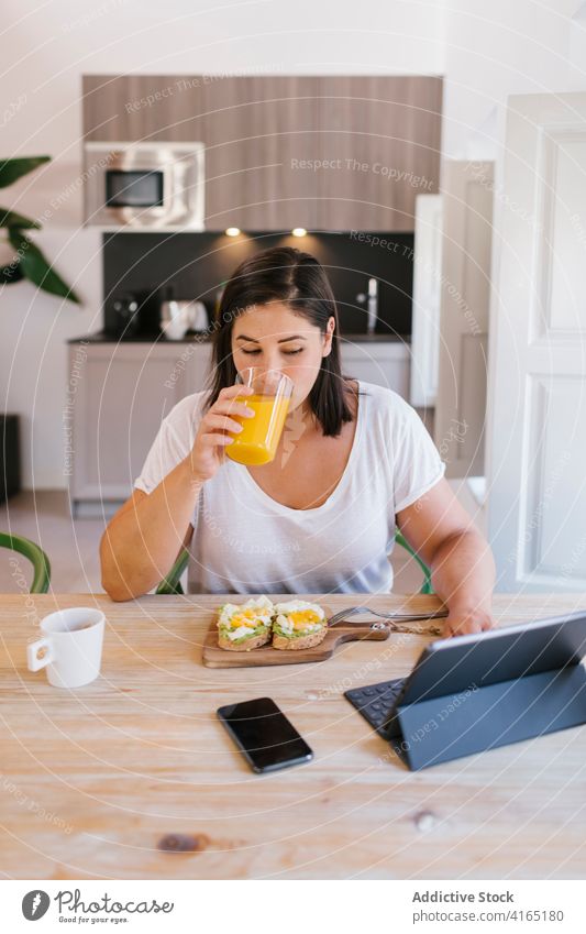 Frau trinkt Orangensaft beim gesunden Frühstück im Innenbereich heimwärts Haus Mädchen Avocado kaufen Küche Kaffee Morgen Kaukasier brünett Tisch Lifestyle