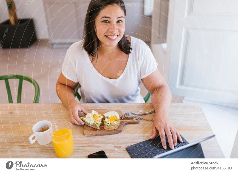 Glückliche und lächelnde Frau beim Frühstück und bei der Arbeit im Innenbereich heimwärts Haus Mädchen Avocado kaufen Küche Kaffee Morgen Kaukasier brünett