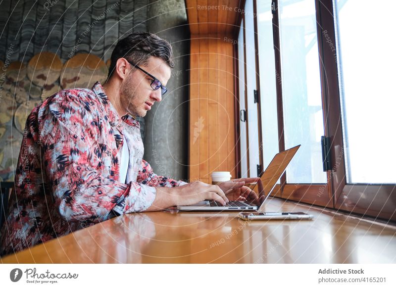 Fernangestellter mit Laptop im Café abgelegen Arbeiter trendy selbstbewusst Fokus Fenstersims Mann Freiberufler Internet Apparatur Gerät online Netbook