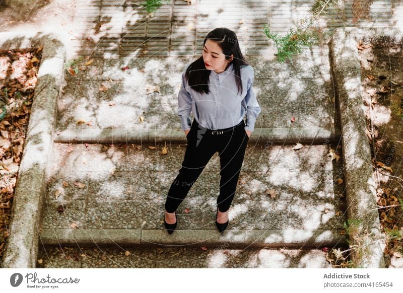 Elegante junge ethnische Dame ruht sich im Herbst Park Frau Stil Treppe elegant Hand-in-Tasche gut gekleidet sich[Akk] entspannen besinnlich Mode Natur