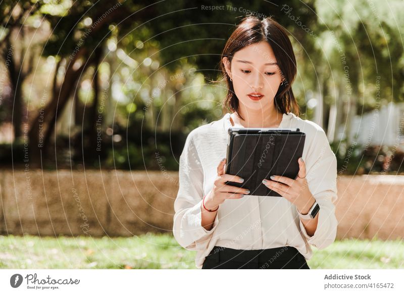 Junge ethnische Frau arbeitet aus der Ferne auf Tablet im Park Arbeit Tablette abgelegen achtsam neue Normale Coronavirus Job beschäftigt Apparatur benutzend