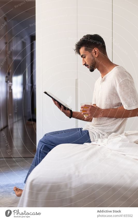 Junger Mann mit Tablet im Schlafzimmer Morgen Tablette benutzend trinken Apparatur Bett zu Hause Gerät jung Vollbart Browsen Internet lesen online Lifestyle