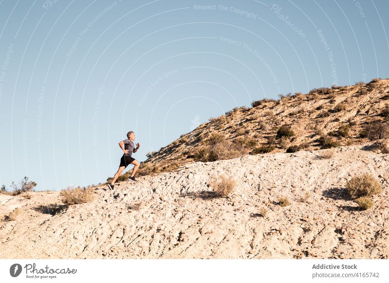 Sportler beim Joggen auf sandigem Untergrund in bergigem Gelände Mann laufen Halbwüste Hügel Training aktiv Jogger Gesundheit Natur Wohlbefinden Sand Übung
