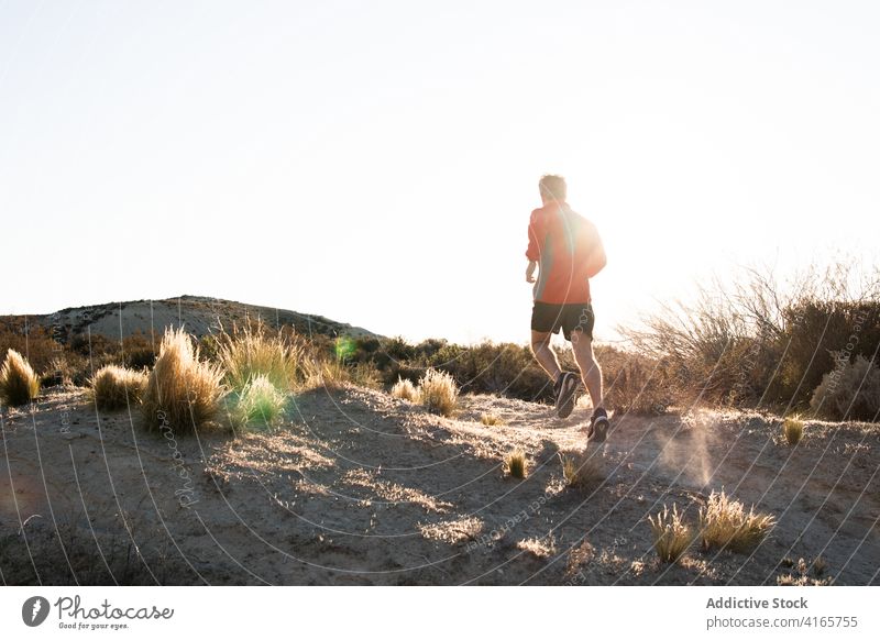 Anonymer Sportler beim Joggen auf sandigem Untergrund in bergigem Gelände Mann laufen Halbwüste Hügel Training aktiv Jogger Gesundheit Natur Wohlbefinden Sand