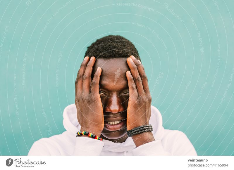 Porträt der jungen afrikanischen schwarzen Mann gegen eine grüne Wand mit weißen Sweatshirt mit den Händen auf seinem Gesicht. Stop Rassismus Protest Konzept. BLM