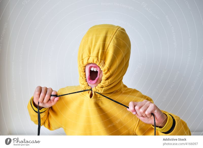 Ausdrucksstarker Teenager im gelben Kapuzenpulli im Studio auflehnen schreien Gesicht machen Farbe Mund geöffnet hell pulsierend Deckblatt verrückt Energie