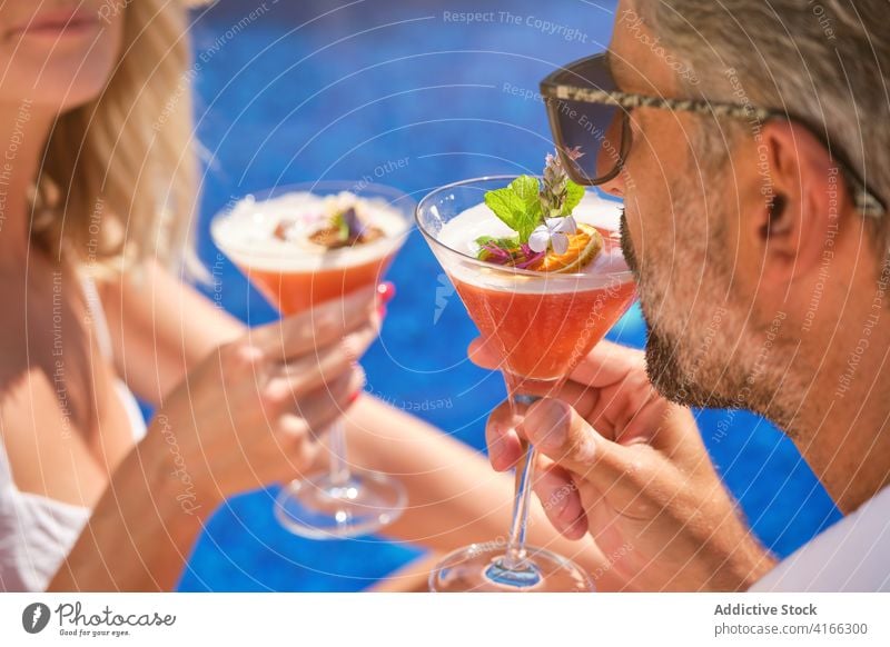 Unbekanntes Paar ruht sich am Swimmingpool mit Cocktails aus Klirren trinken Beckenrand genießen Glück Liebe Partnerschaft sich[Akk] entspannen Urlaub Feiertag