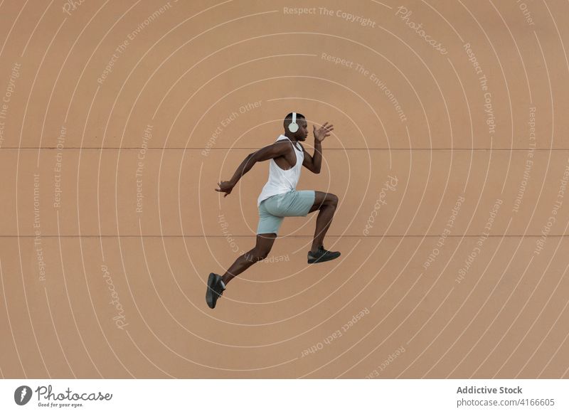 Schwarzer Sportler läuft beim Training auf der Straße springend Läufer Herz Aktivität Kopfhörer üben Übung Motivation Fitness Mann Lifestyle laufen Gesundheit