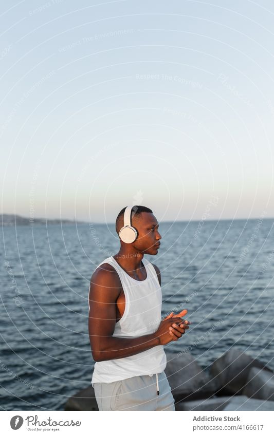Schlanker schwarzer Mann an der Strandpromenade beim Training Läufer Hafengebiet Aufwärmen Kopfhörer Dehnung Energie Konzentration Wohlbefinden männlich