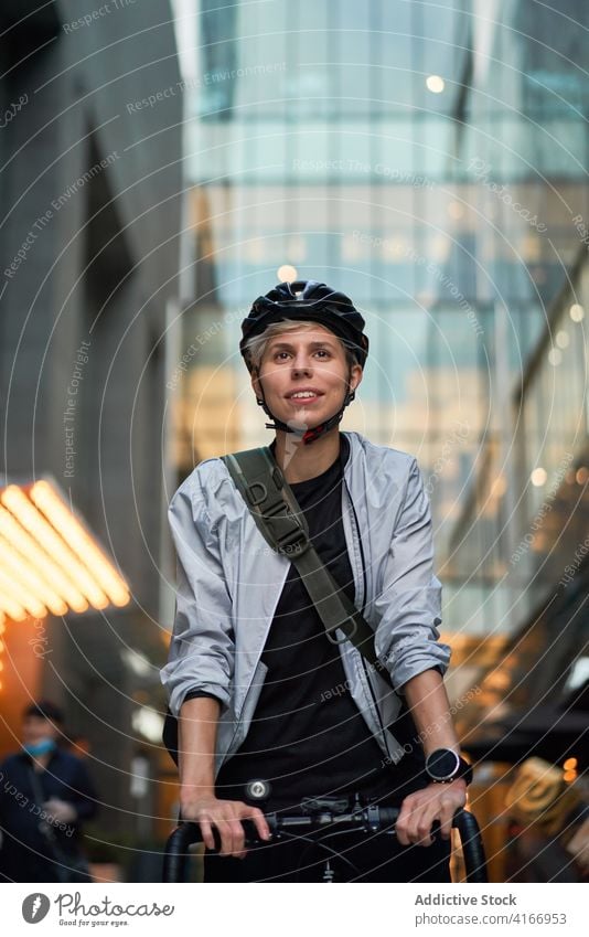 Frau mit Helm auf dem Fahrrad in der Nähe eines hohen Gebäudes mit Glasfenstern Radfahrer gemauert Großstadt Tag jung Sport Reiten Sommer Schutzhelm schützend