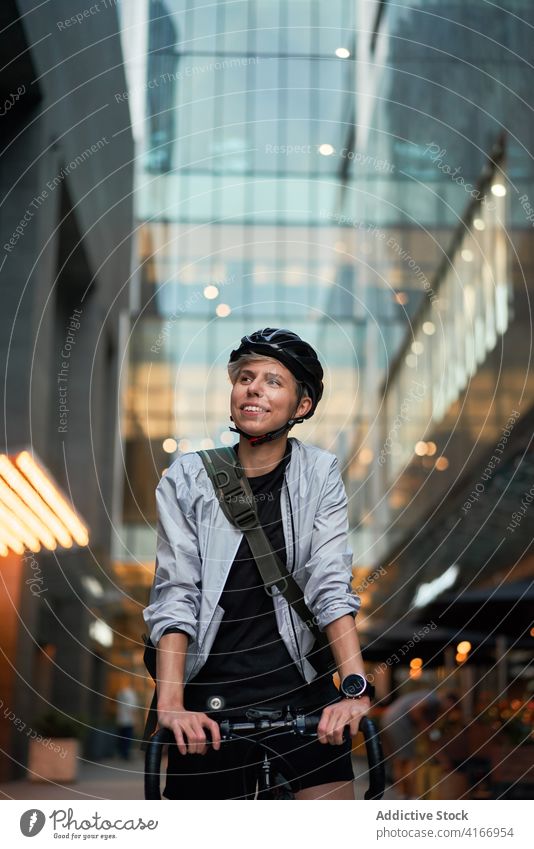 Nahaufnahme einer Frau mit Helm auf einem Fahrrad, die in der Nähe eines hohen Gebäudes zur Seite schaut Radfahrer gemauert Großstadt Tag jung Sport Reiten
