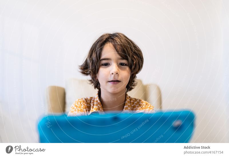 Konzentrierter Junge schaut zu Hause auf den Laptop zuschauend Internet online Kindheit Fokus Tisch heimwärts benutzend Apparatur Gerät Netbook modern Stil hell