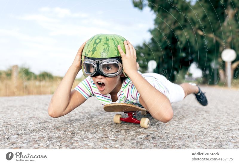 Positives Kind auf Skateboard in Schutzbrille und dekorativem Helm Junge Spaß haben Brille Schutzhelm sorgenfrei genießen Mund geöffnet Aktivität Straße