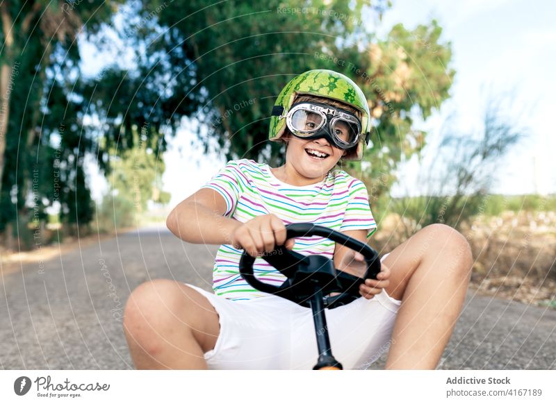 Aufgeregter Junge fährt Tretauto auf der Straße Mitfahrgelegenheit erstaunt Erholung Spaß haben Aktivität aufgeregt Schutzbrille Kindheit trendy anhaben Go-Kart