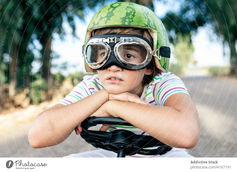 Melancholisches trendiges Kind mit Brille und Wassermelone als Kopfbedeckung Junge Melancholie Schutzbrille trendy verträumt Lenkrad sich auf die Hand lehnen