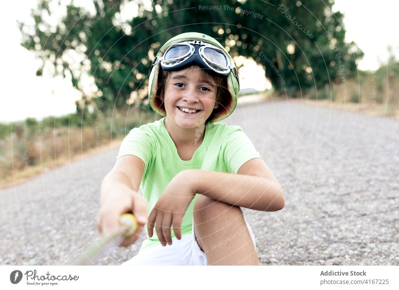 Fröhlicher Junge auf dem Skateboard, der ein Selfie mit seinem Smartphone macht Schutzhelm Brille froh Kindheit Freizeit Straße benutzend Apparatur Gerät