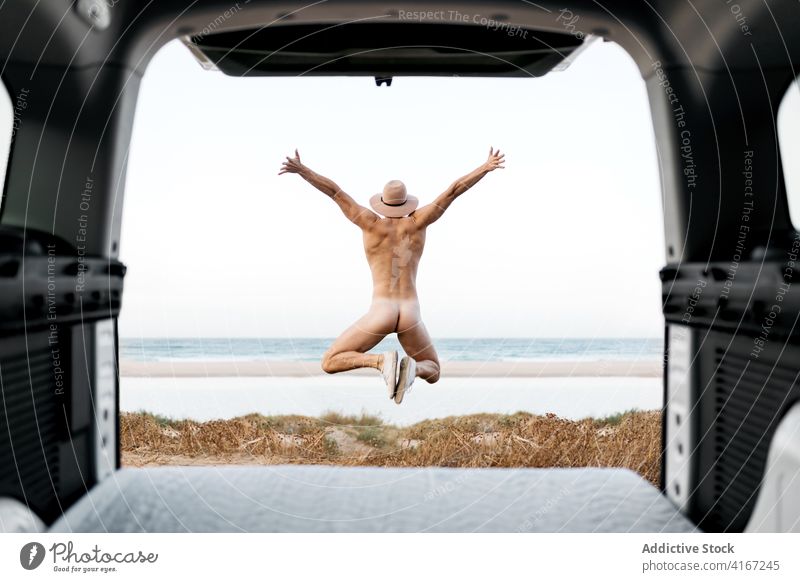 Anonymer nackter Mann mit ausgestreckten Armen in Aufregung am Meeresufer ausdehnen Freiheit springen Meeresküste Freude reisen aufgeregt Stiefel PKW Autoreise