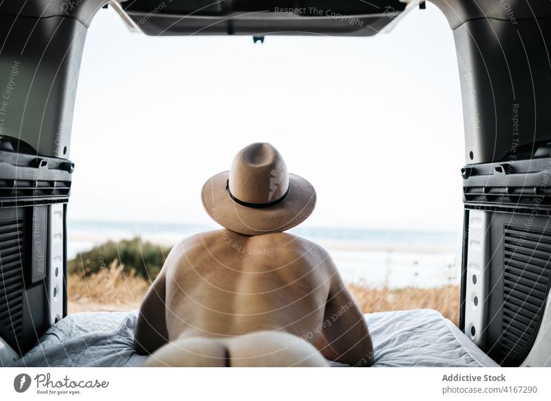 Unerkennbarer nackter Mann mit Hut, der auf einer Matratze in einem Fahrzeug ruht Tourist nachdenken Meer Schlafmatratze Urlaub Himmel Lügen Horizont endlos