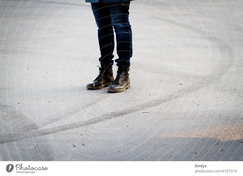 weibliche Person mit Springerstiefeln steht auf einem leeren Platz umgeben von Reifenspuren eines driftenden Autos Frau Beine Asphalt Dynamik verlassen