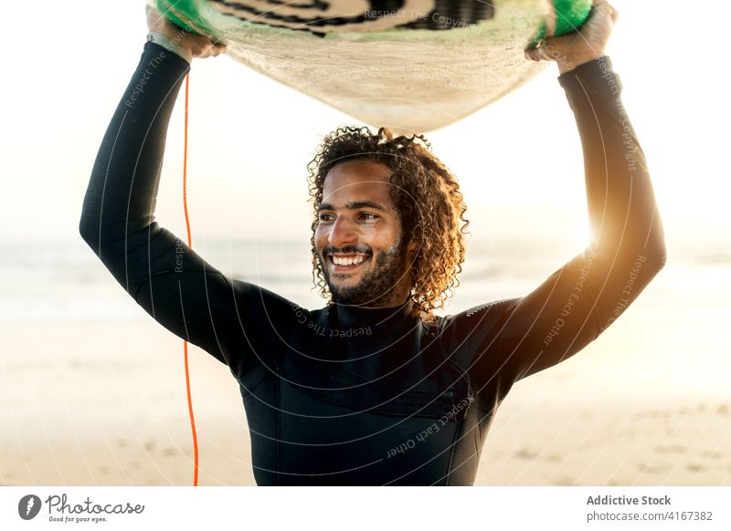 Fröhlicher Surfer hält Skimboard über den Kopf Mann heiter Sonnenuntergang Meeresufer Freiheit tropisch Wassersport männlich Resort ethnisch MEER Strand Sommer