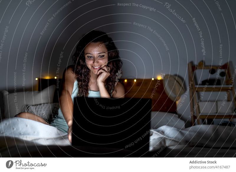 Charmante Frau sieht sich im Schlafzimmer einen Film auf dem Laptop an zuschauen heimwärts dunkel Kälte benutzend unterhalten Bett Video lustig ruhen Apparatur