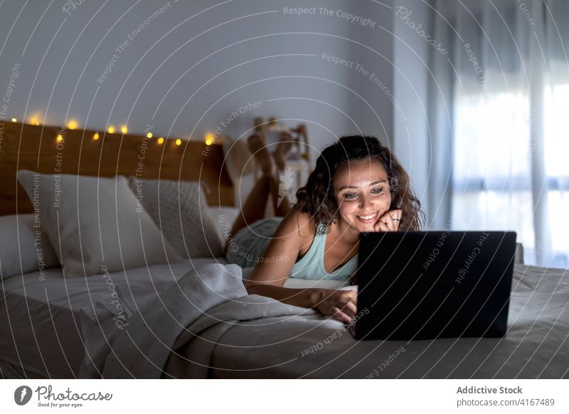 Charmante Frau sieht sich im Schlafzimmer einen Film auf dem Laptop an zuschauen heimwärts dunkel Kälte benutzend unterhalten Bett Video lustig ruhen Apparatur