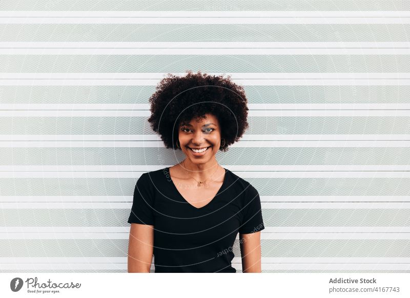 Afro-Frau schaut in die Kamera und lacht gegen eine weiße Wand schwarz Porträt schön Menschen Afrikanisch Glück Afro-Look jung lässig heiter Mädchen Gesicht