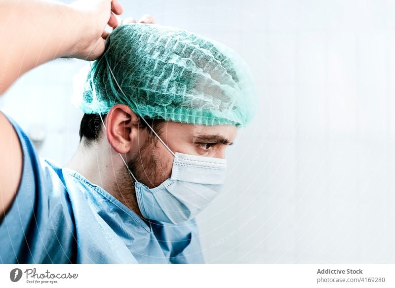 Medizinisches Fachpersonal setzt vor der Behandlung eines Patienten eine Maske auf Sanitäter Chirurg Mundschutz angezogen vorbereiten steril Mann medizinisch