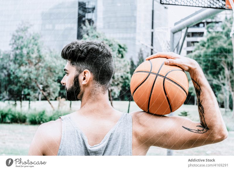 Sportlicher Mann mit Basketball auf der Straße Ball Spieler selbstbewusst sportlich Vollbart spielen Streetball männlich jung Tattoo muskulös Athlet urban