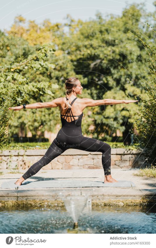 Frau balanciert in Krieger-Yoga-Pose im Park Baum virabhadrasana Gleichgewicht stehen üben positionieren Asana passen Wellness schlank Körperhaltung Energie
