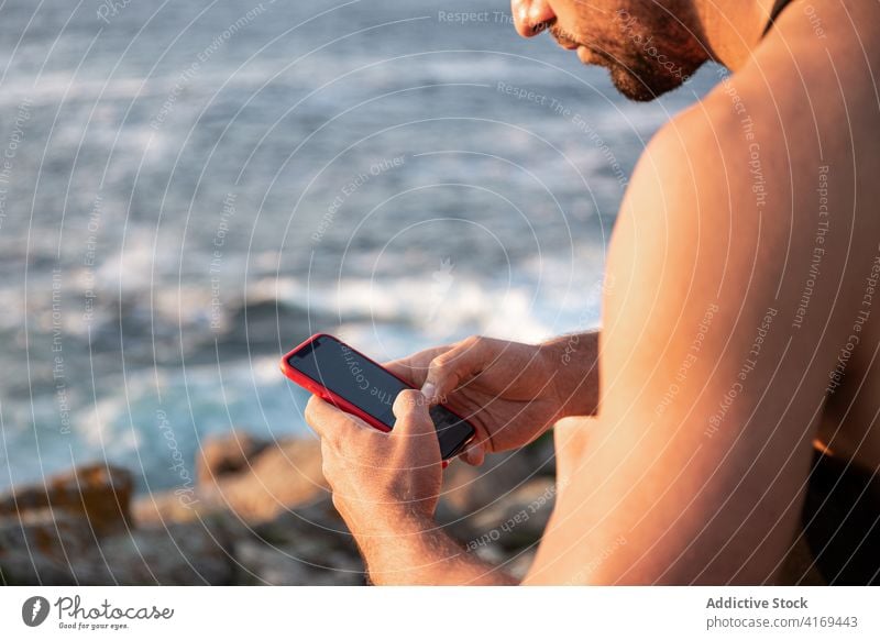 Mann sitzt am Meeresufer und surft auf seinem Smartphone Browsen soziale Netzwerke Surfen sich[Akk] entspannen unterhalten Sonnenuntergang MEER männlich Sommer
